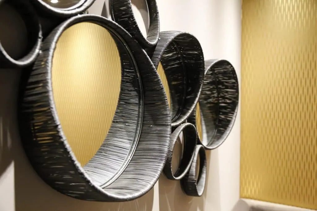 Close-up of round mirrors with thick black frames reflecting the gold wallpaper