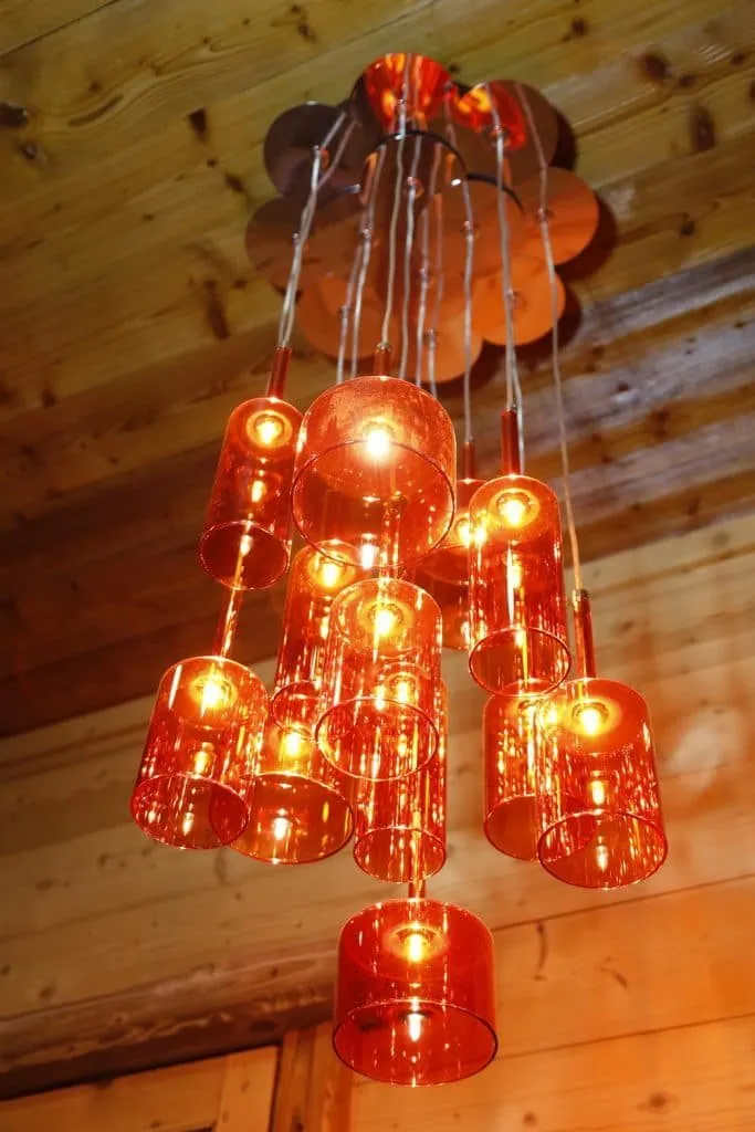 Cluster pendant light of orange glass cylinders beneath the bar’s wooden ceiling