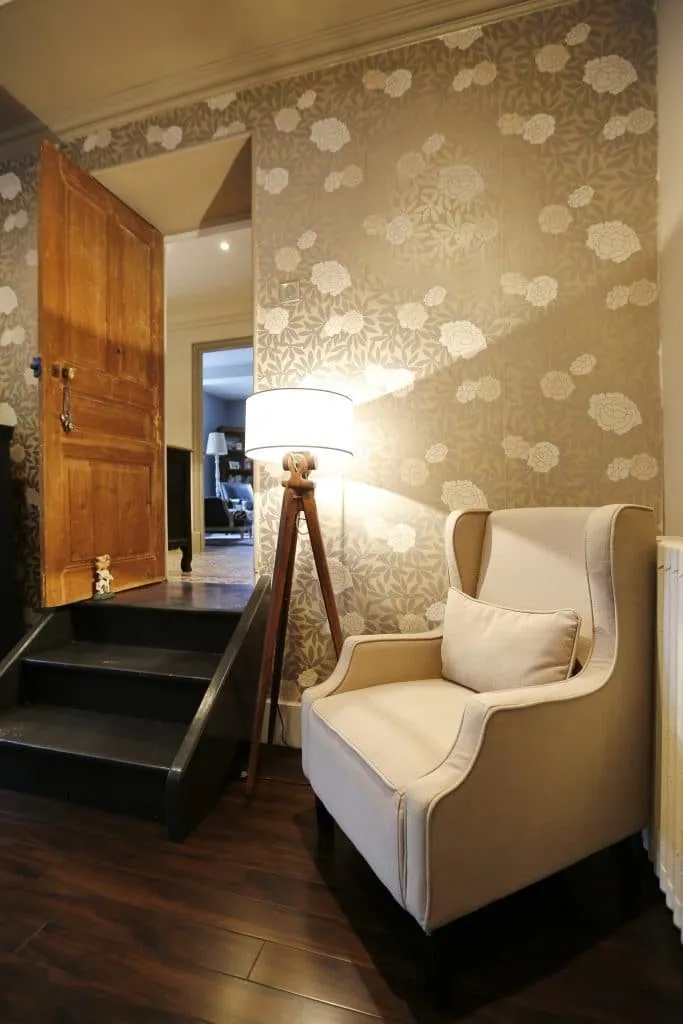 Cream wingback armchair and wooden tripod floor lamp against wallpaper with large flowers