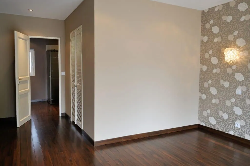 Former garage turned bedroom in Rhône-Alpes: dark parquet, floral wallpaper and louvred doors
