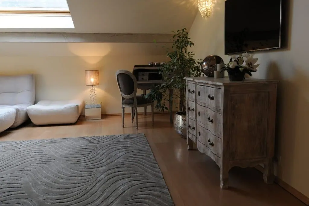 Desk corner, weathered chest of drawers and wave-patterned grey rug in the attic bedroom