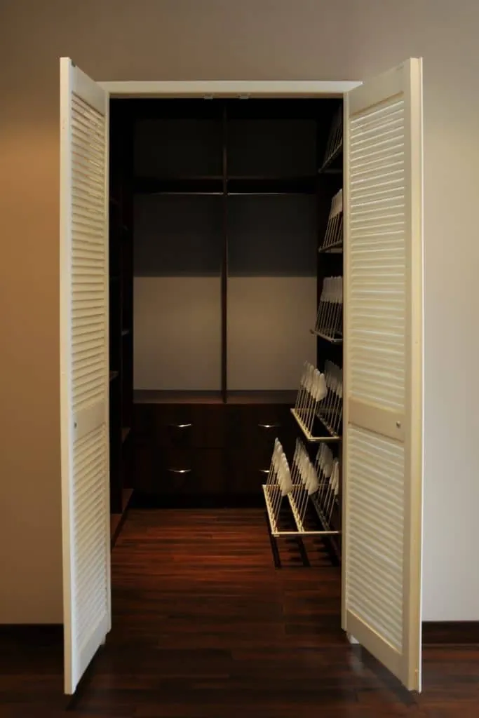 Bespoke dressing room behind white louvred doors, with dark wood shelving and shoe racks
