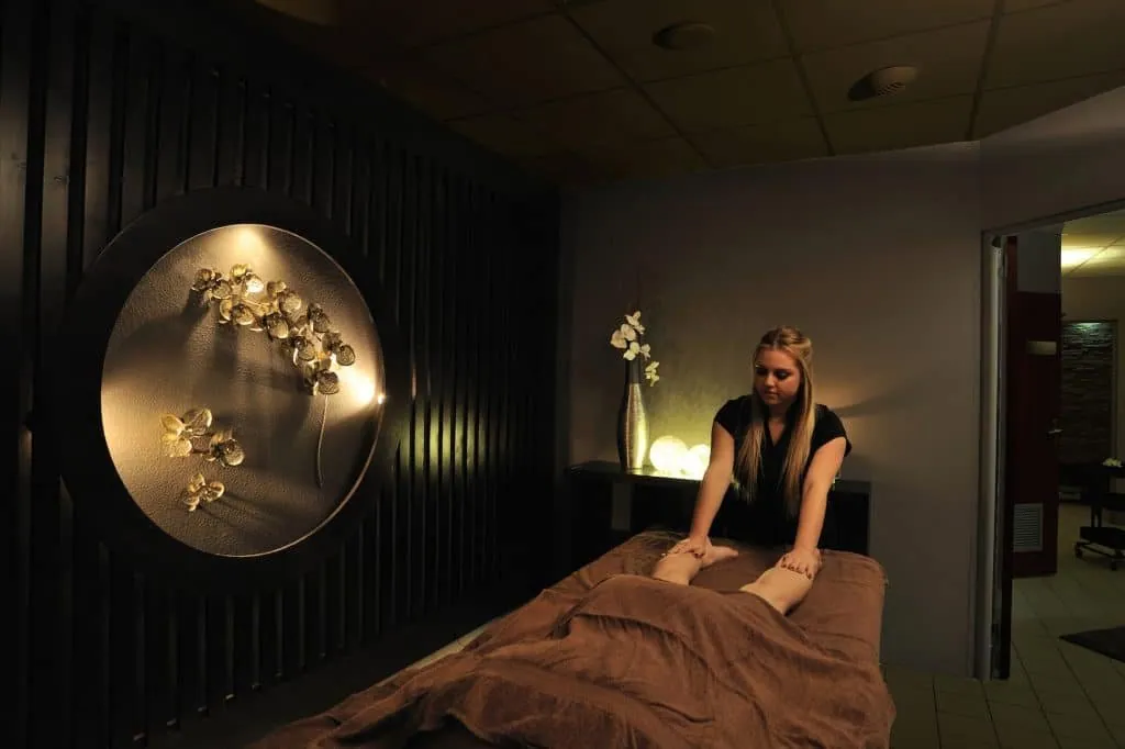 Massage in a treatment room, round illuminated niche with golden orchids, dark slatted wood wall