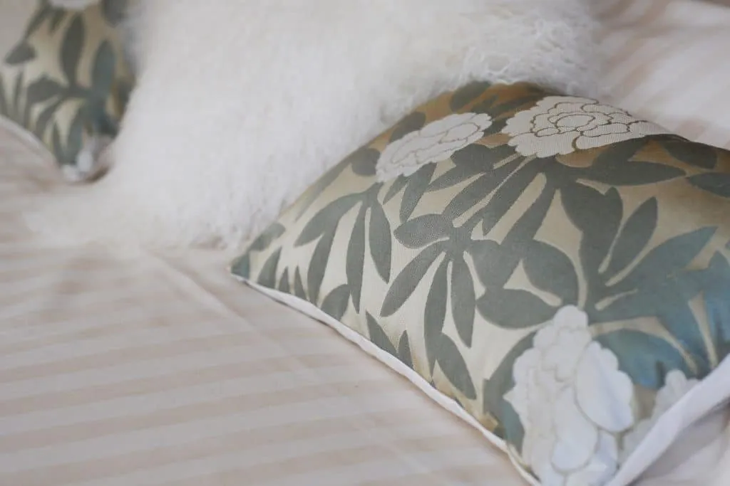 Sage green floral cushions and a fluffy white cushion on the bed