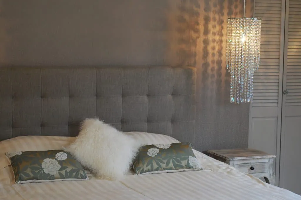 Grey tufted headboard, cushions and a crystal pendant light above the bedside table