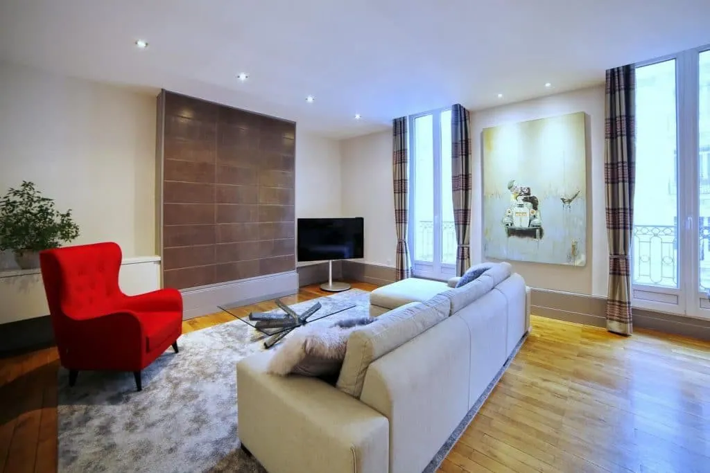 Living room in a Grenoble apartment: leather wall panels, red armchair and light sofa