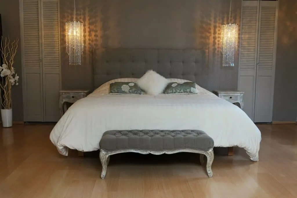 Renovated bedroom with a grey tufted headboard between two crystal pendant lights