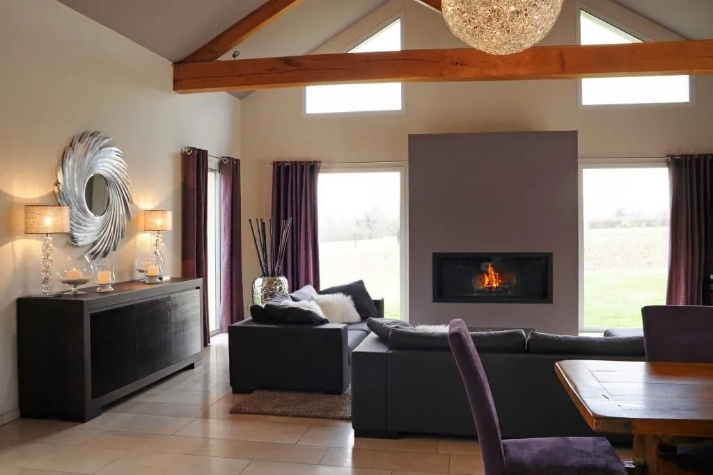 Living room in a Rhône-Alpes home: exposed beam, built-in fireplace, grey sofas and plum curtains
