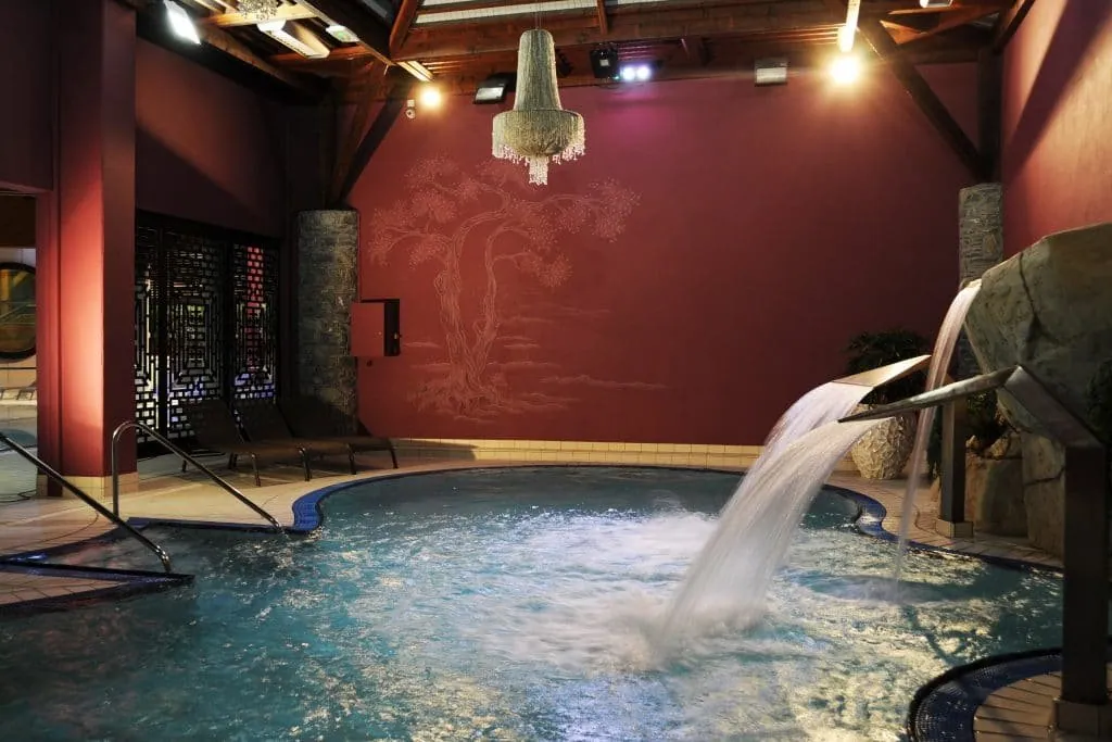 Aqua spa de Val Thorens : bassin à jets d’eau, mur rose foncé peint d’un arbre