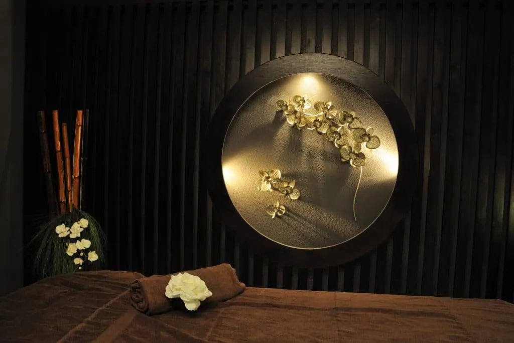 Massage table, rolled towel, white flower, bamboo stems and round niche with golden orchids