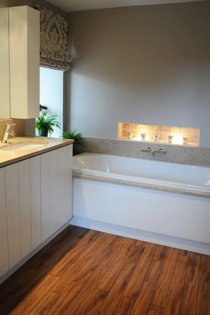 Customised white vanity unit, built-in bath, lit niche and warm-toned wooden floor