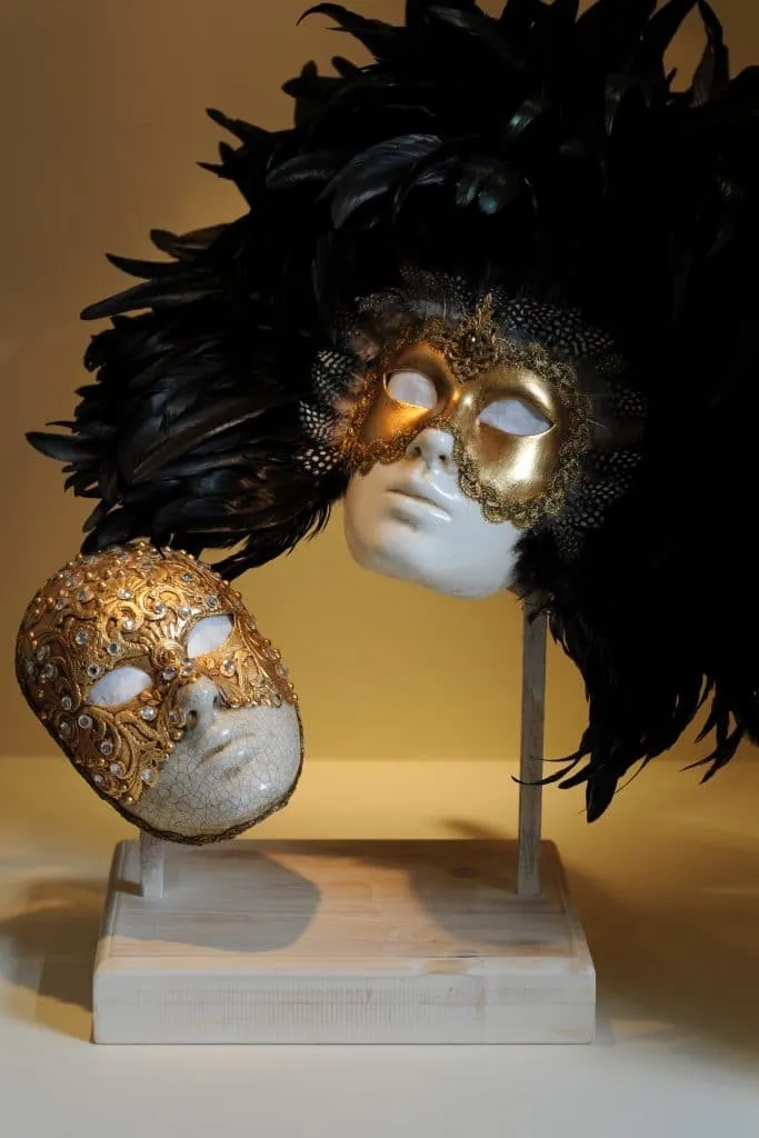 Gold Venetian masks with black feathers on a wooden stand, part of the bedroom decor
