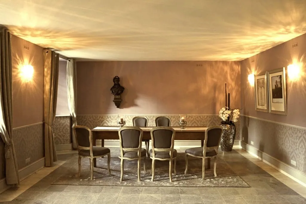 Large table on a grey rug, wall-mounted bust, taupe curtains and glowing wall lights