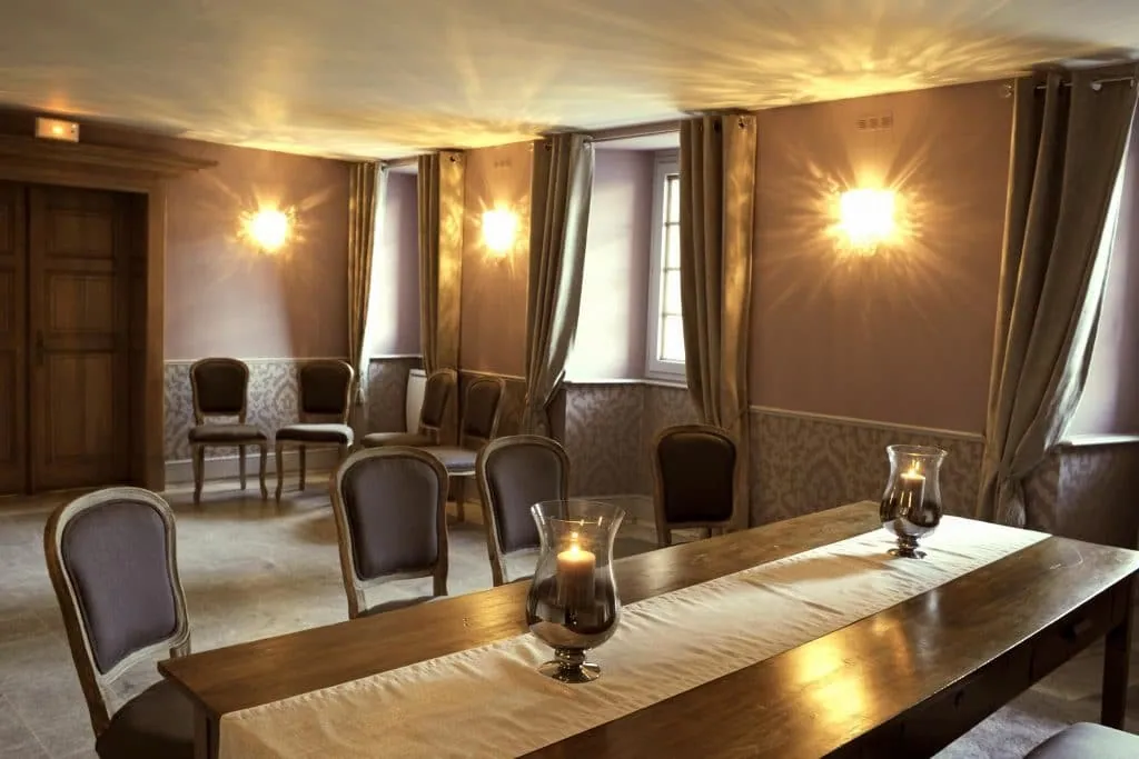 Wedding hall with taupe curtains and glowing wall lights, wooden table and lit glass candle holders