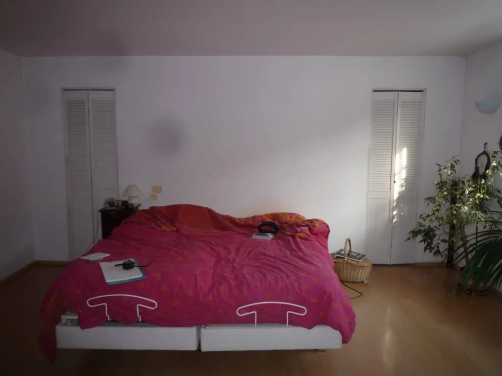 The bedroom before renovation, with white walls, a pink duvet and louvred wardrobes