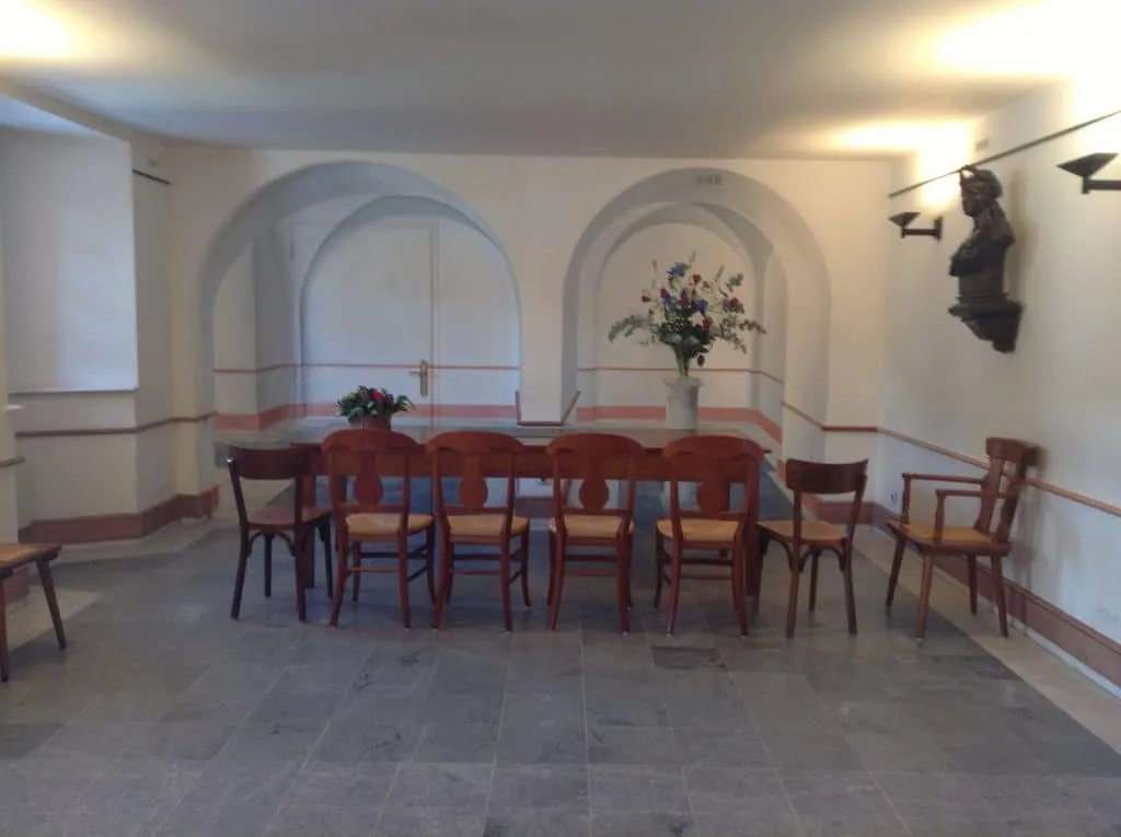 Before the project, table and bistro chairs in front of two white arches, wall-mounted bust
