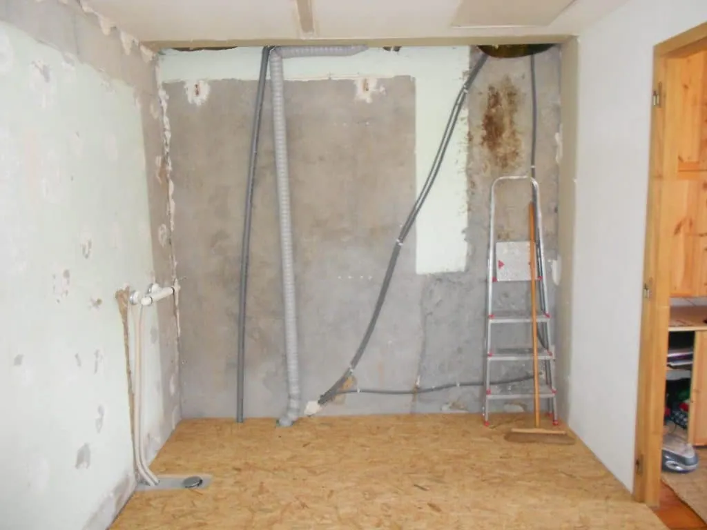 Bathroom before the renovation: bare walls, exposed ducts and pipes, OSB subfloor