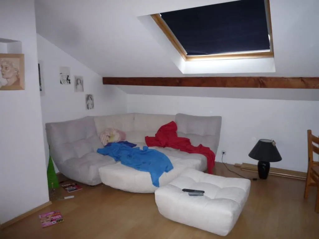 The sofa corner before renovation, beneath a brown wooden beam and a skylight