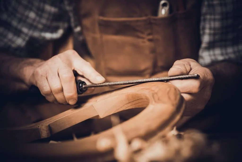 Craftsman shaping a curved wooden piece with a file, bespoke furniture design