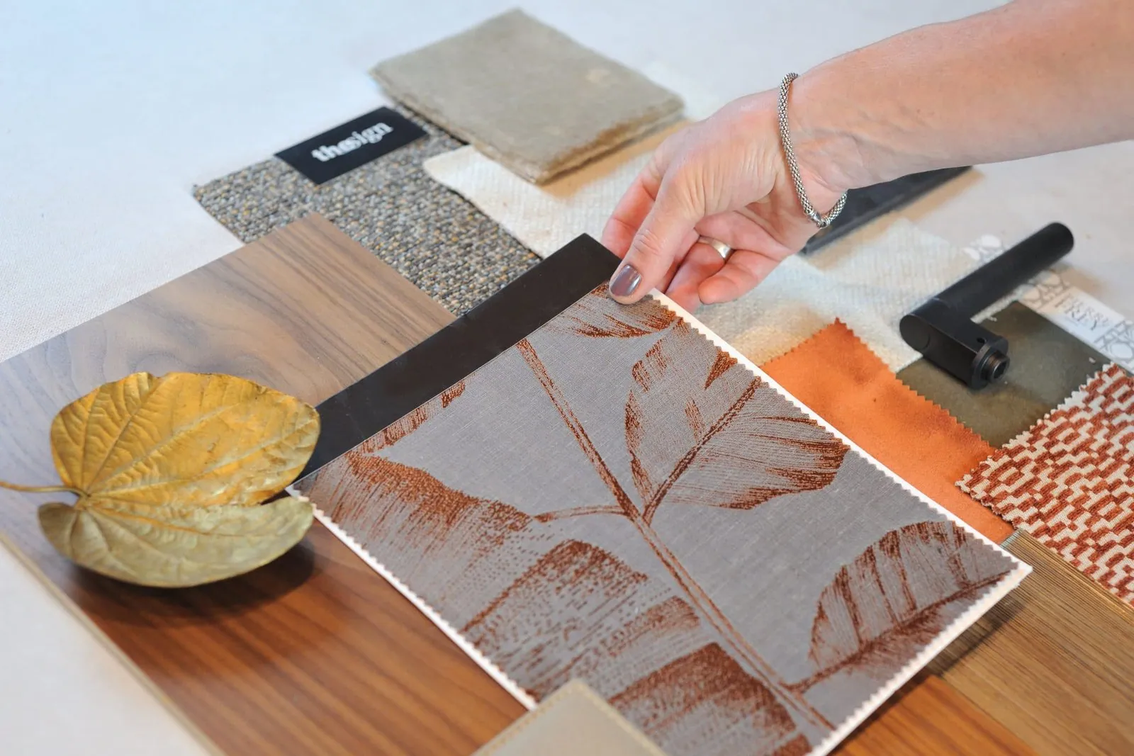 Hand arranging a mood board combining wood, orange velvet and copper leaf-print fabric