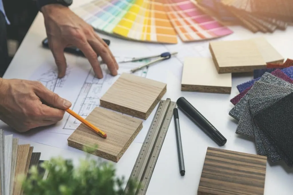 Project management, working on plans surrounded by colour swatches, wood and carpet samples