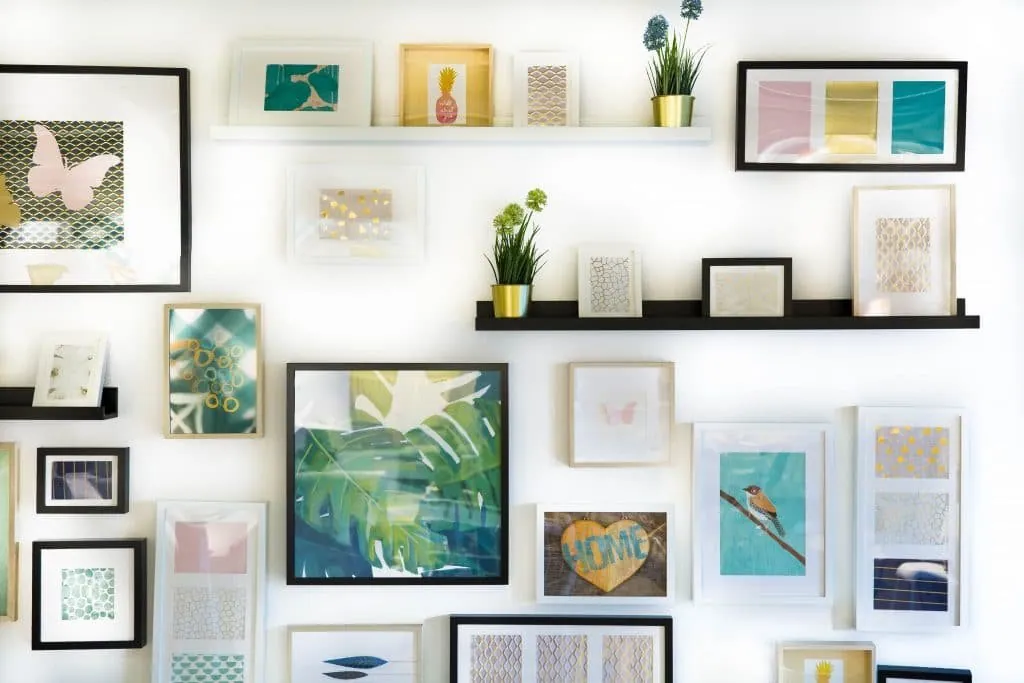 Picture wall mixing colourful prints in black, white and wooden frames, with shelves and plants
