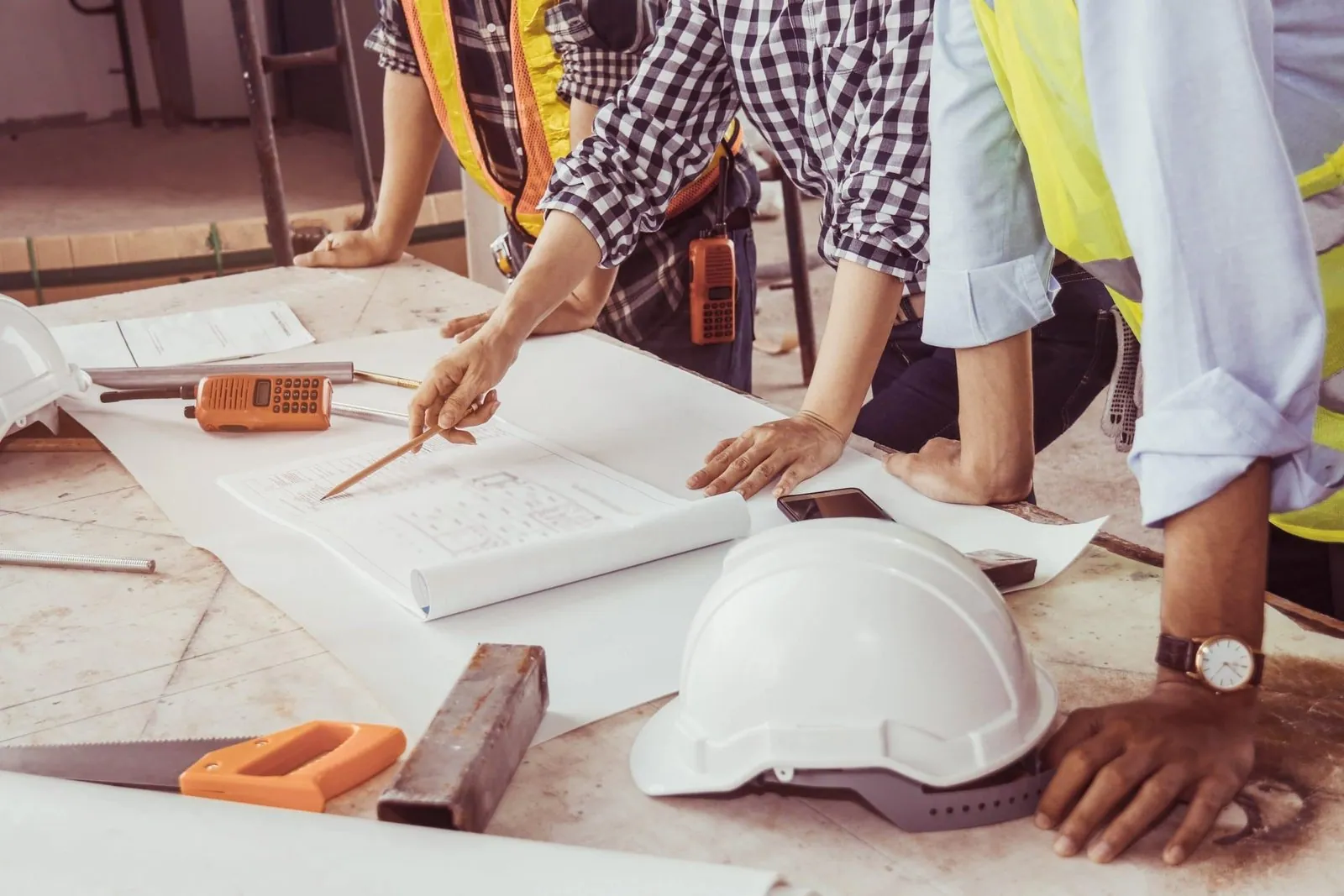 Building professionals leaning over site plans, a white hard hat on the table