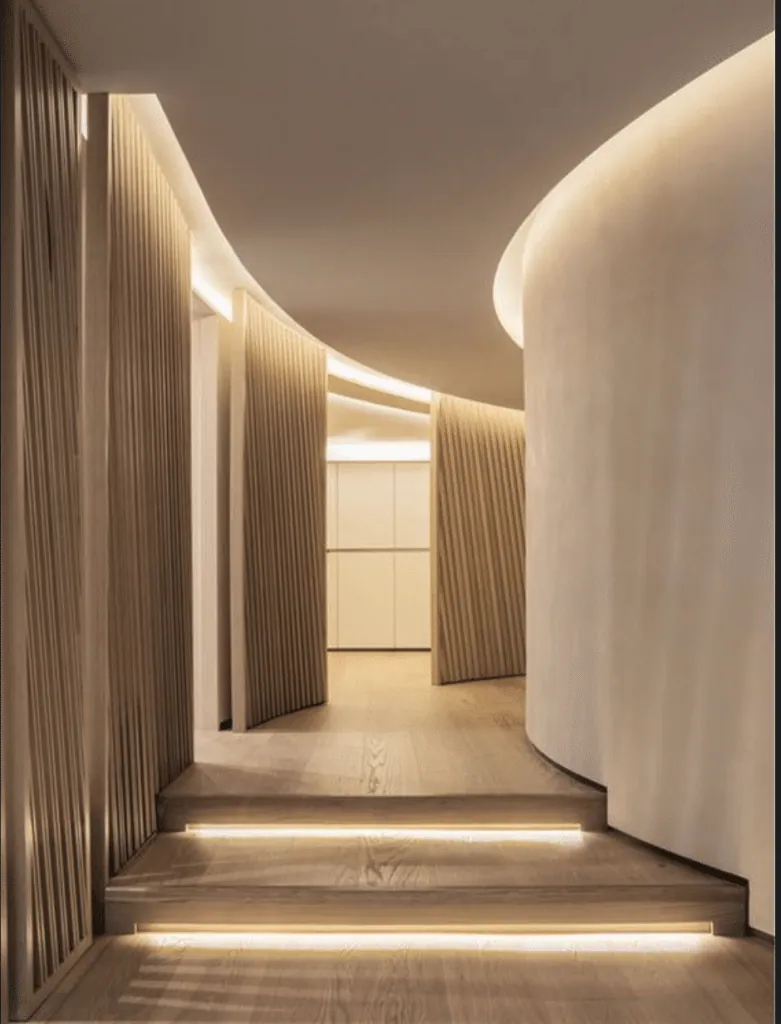 Curved light-wood hallway with indirect ceiling lighting and LED strips beneath the steps