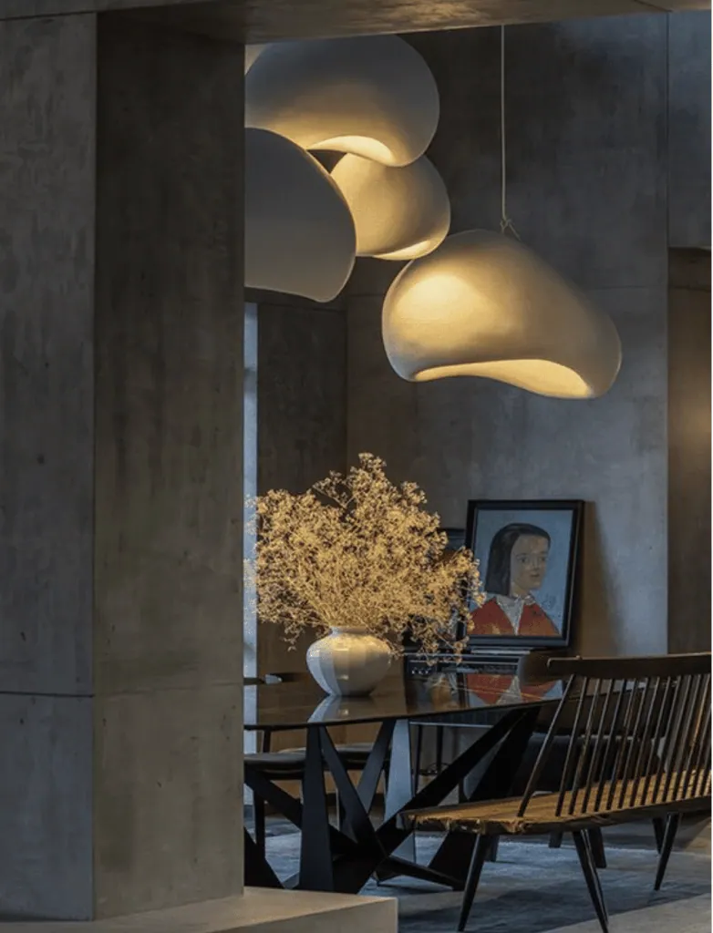 Raw concrete dining room lit by white pendant lights with organic shapes