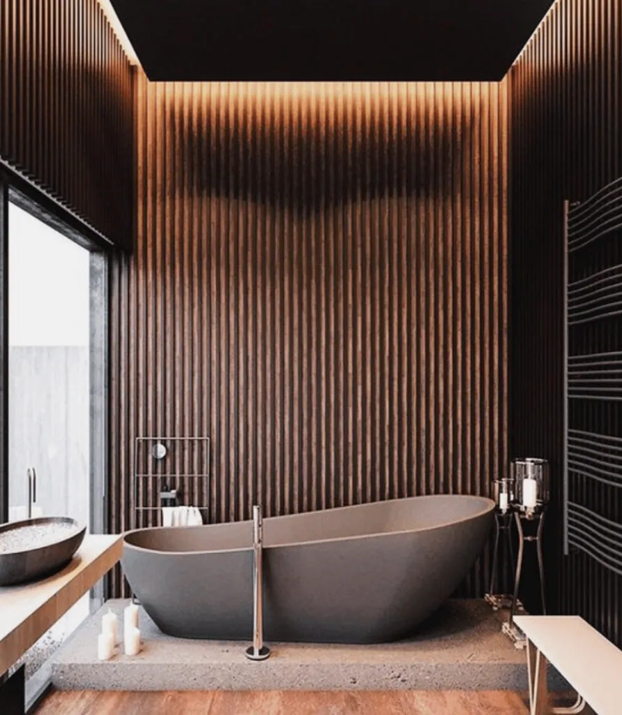 Dark wood slatted bathroom with grazing light and a grey freestanding bathtub on a plinth