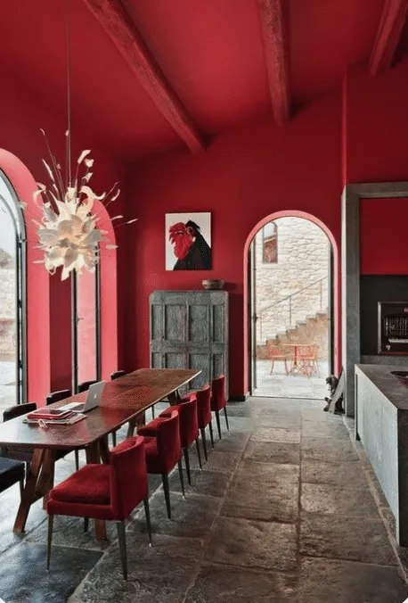 Dining room with red walls, exposed beams, velvet chairs and a stone floor