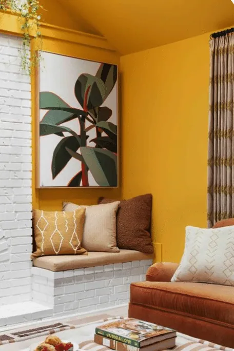 Mustard yellow nook with a white brick bench seat, cushions and a botanical painting