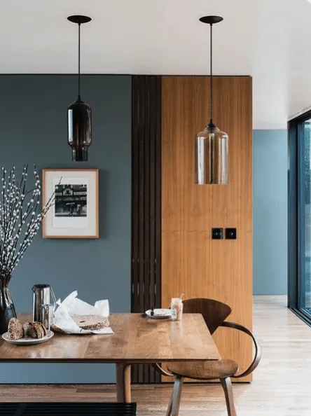Dining area with a blue-grey wall, glass pendant lights and a wooden table