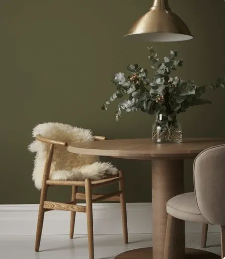 Olive green dining corner with a round wooden table, gold pendant light and eucalyptus