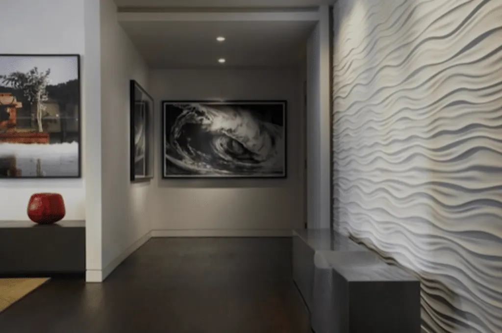 Couloir au mur blanc sculpté en vagues, parquet sombre et œuvres encadrées