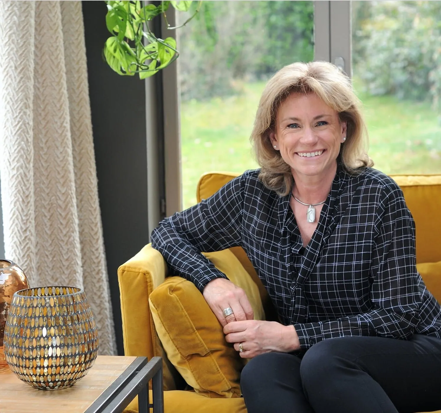 Lisa Paunovitch on a mustard velvet sofa by a large window onto the garden