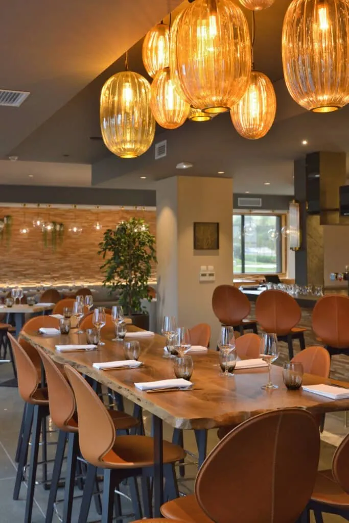 Longue table haute en bois au bord naturel, sous les suspensions ambrées du restaurant Le 205