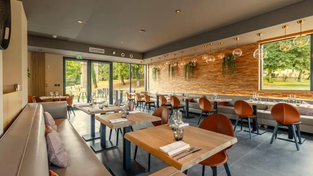 Le 205 dining room with a long grey banquette and large windows overlooking the trees