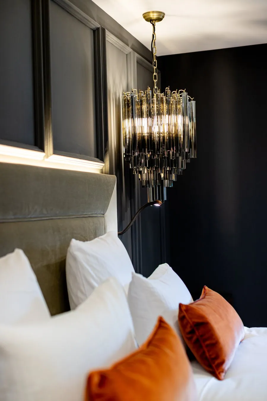 Détail d'une tête de lit, coussins orangés et lustre